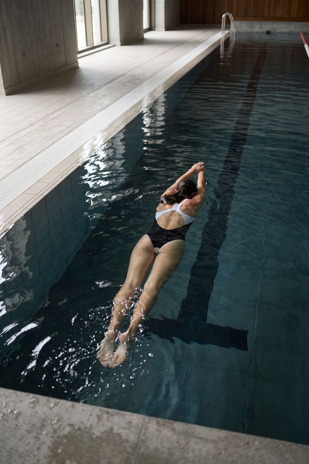 Woman swimming backstroke in an indoor pool wearing the black and white Liberty racerback swimsuit