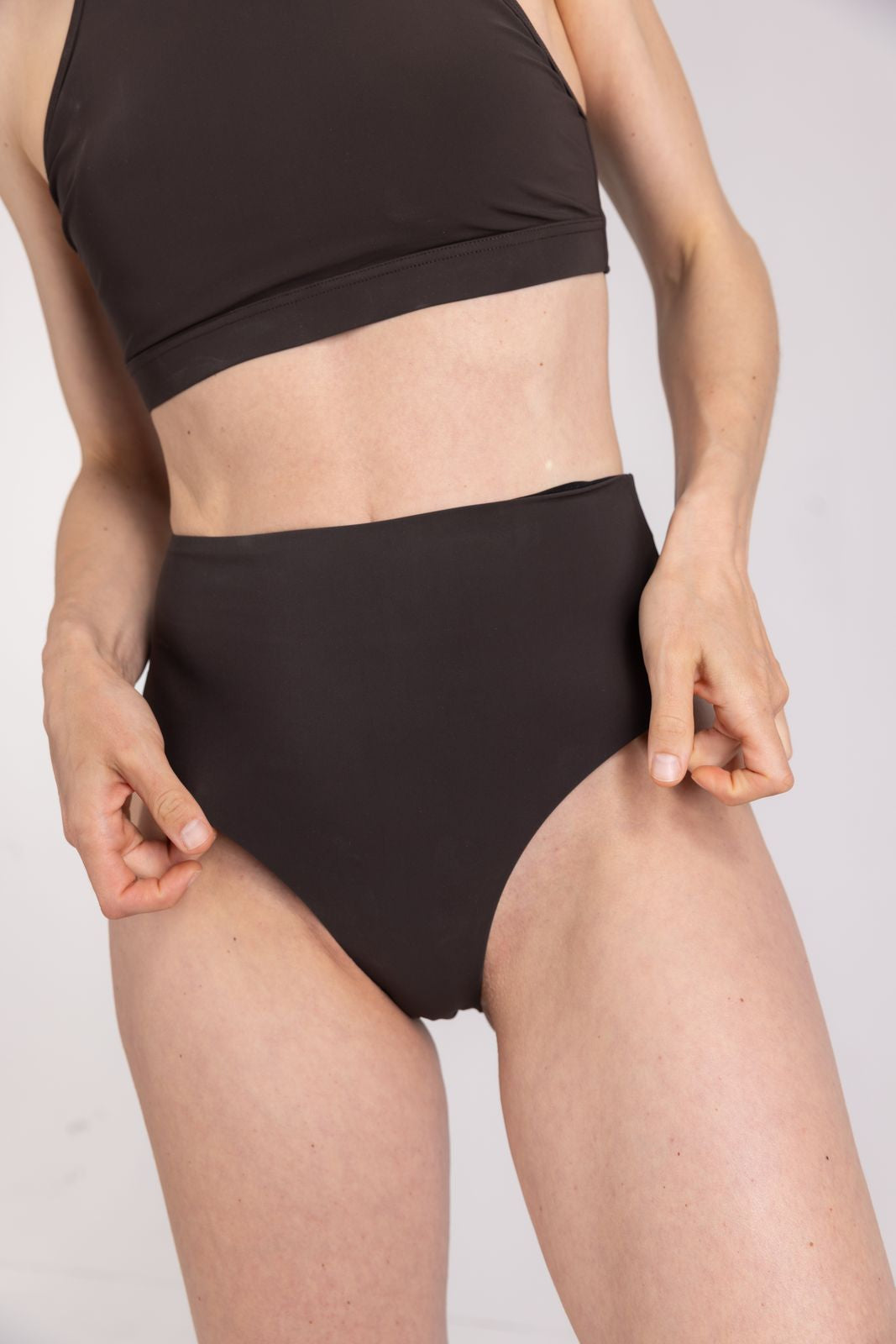 Detail close up of eco-friendly high waist coffee bikini bottom with stretch fabric and sleek finish, on white background