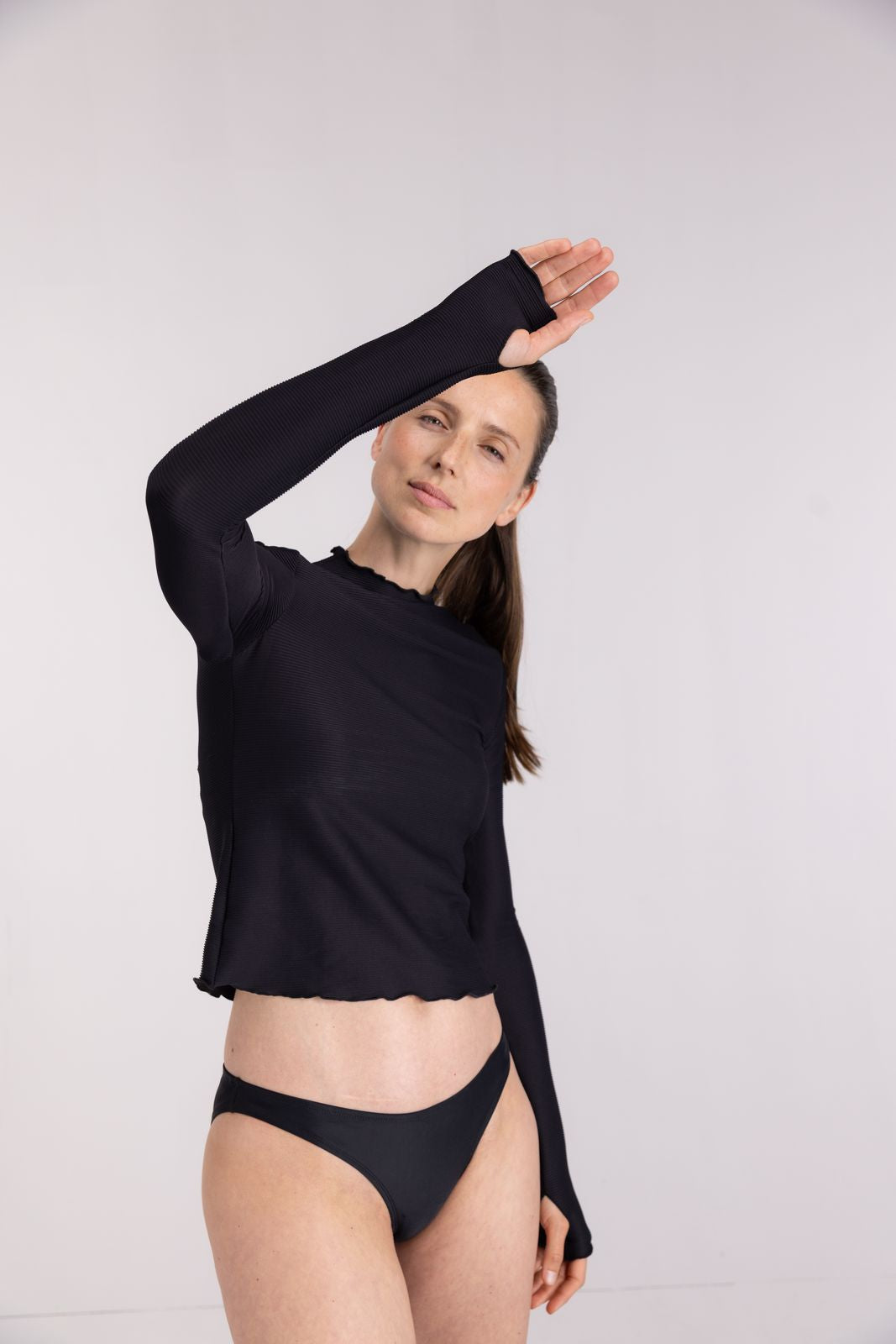 Model raising arm in black WALLIEN rash guard with textured finish, sun-ready protection for beach workouts, studio setting