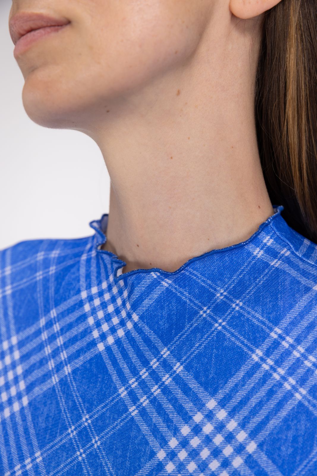 Close-up of blue check rash guard fabric and scalloped collar edge, showing soft eco fabric texture, with studio backdrop