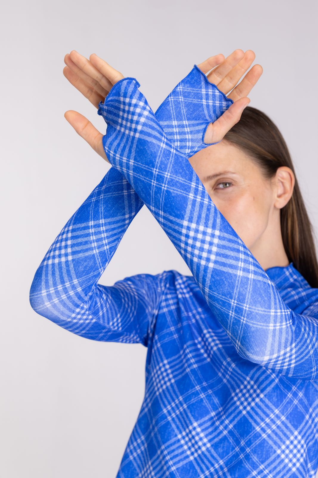 Blue check rash guard sleeves crossed playfully, showcasing flexible long-sleeve design for water sports, on studio backdrop