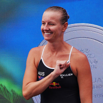 Woman in athletic wear with a branded top, celebrating against a blue background with sports equipment.