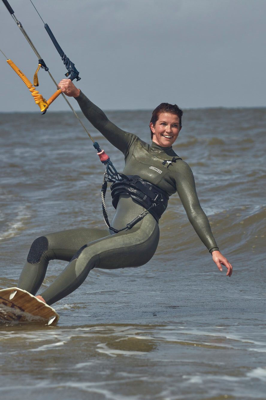 Smiling kitesurfer riding waves in Nikki van Dijk 3/2 wetsuit, for watersports, with kite lines and choppy sea in background