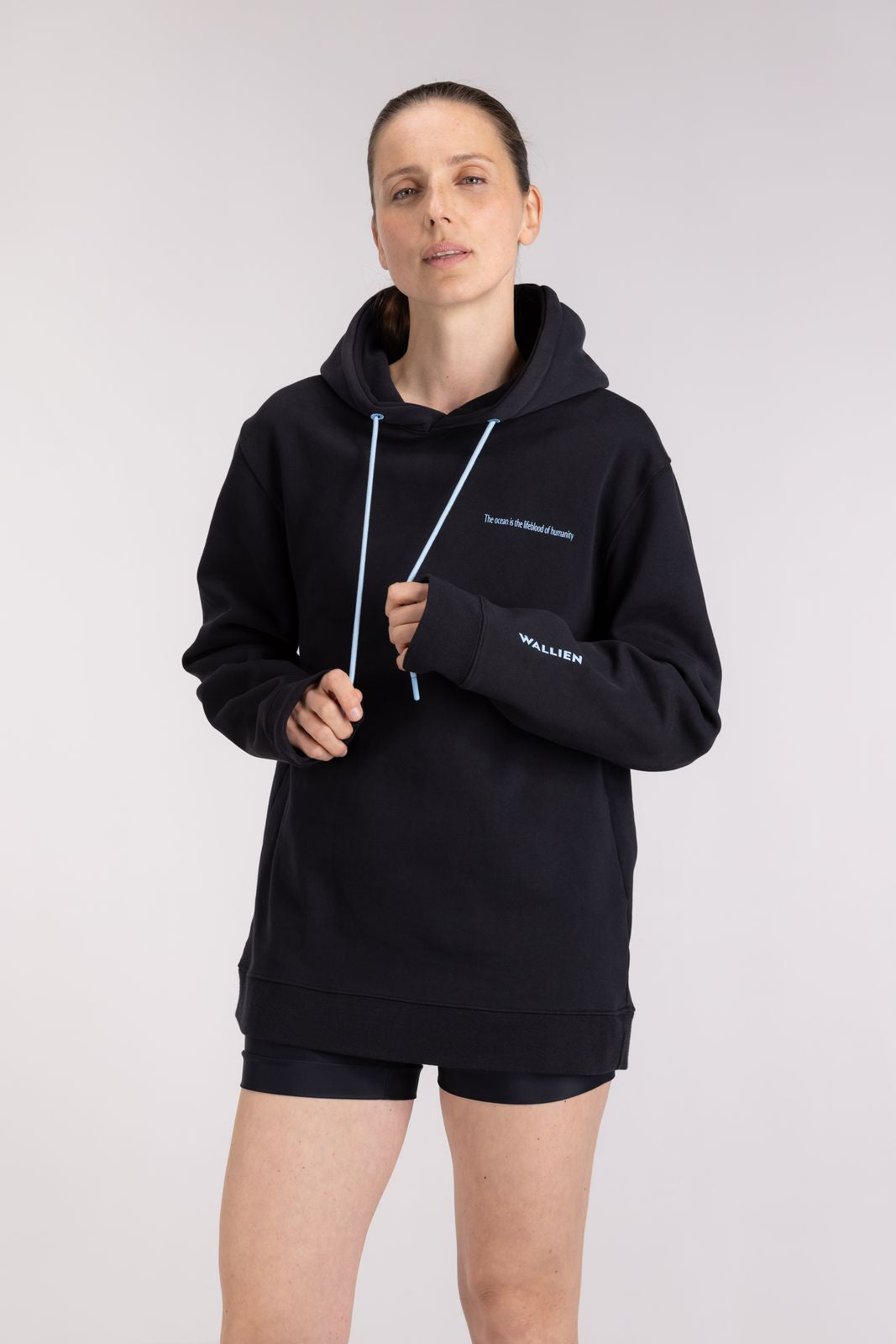 Woman wearing Black Ocean Hoodie for pre-surf warmth, standing confidently indoors on a soft gray studio background