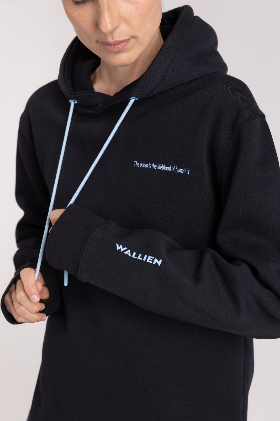 Close-up of WALLIEN Black Ocean Hoodie showing sleeve logo and slogan embroidery, for afterswim session on studio background