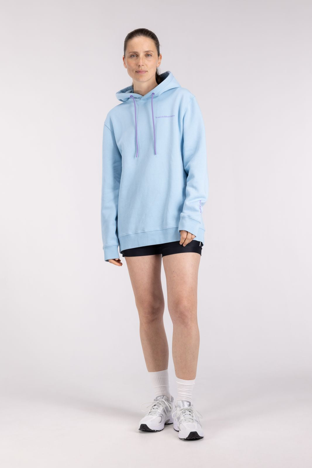Woman wearing the WALLIEN Ocean Hoodie in blue for post-surf warmth, standing casually in studio with light background