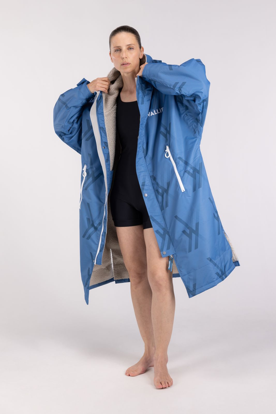 Woman wearing blue WALLIEN changing robe over swimsuit, adjusting collar after swim, with light studio background