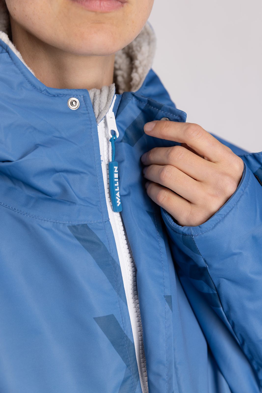 Close-up of WALLIEN zipper and logo detail on blue changing robe, sherpa lining visible, studio light background