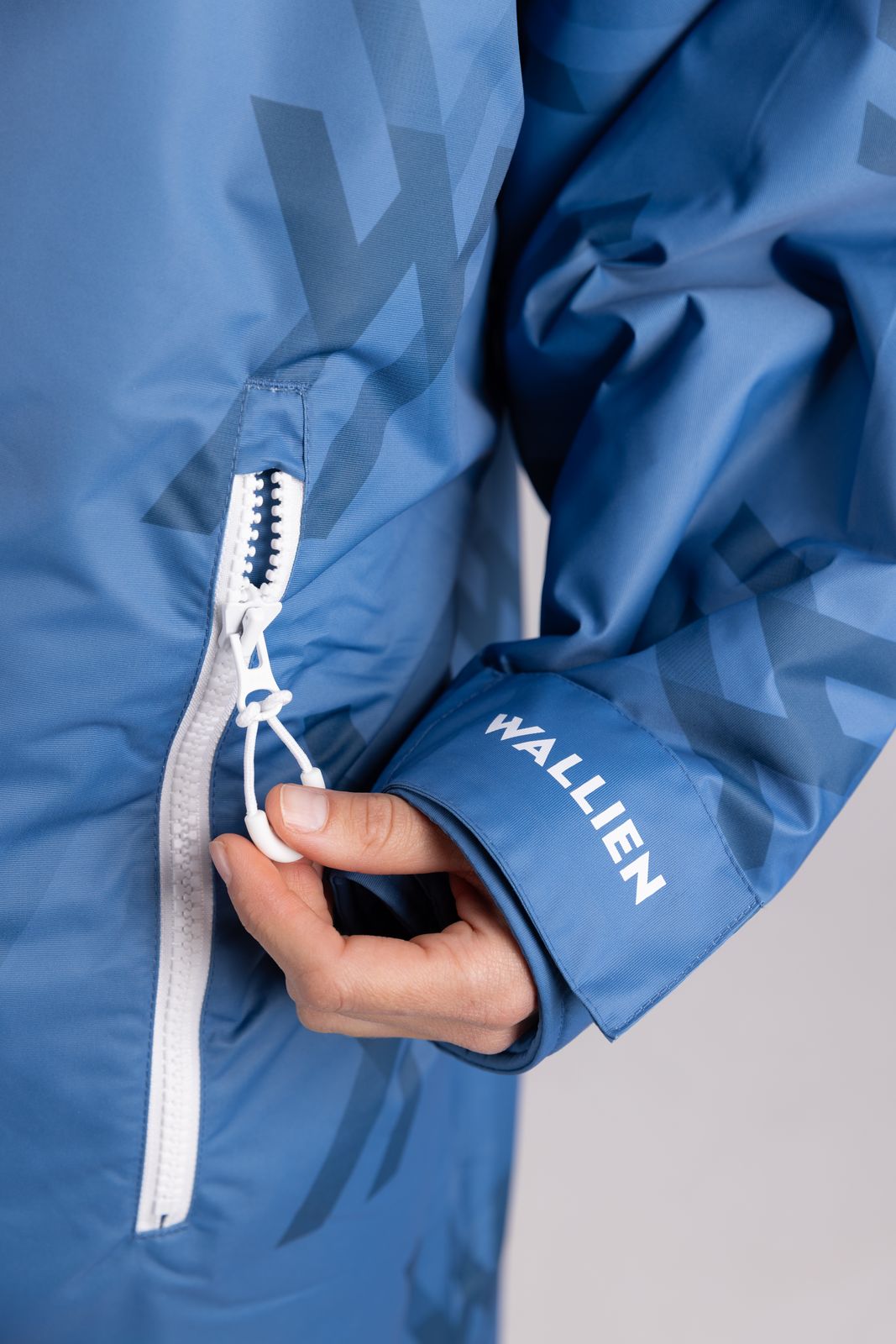Close-up of WALLIEN changing robe sleeve with branding and zip pocket detail, hand holding drawstring, on studio background