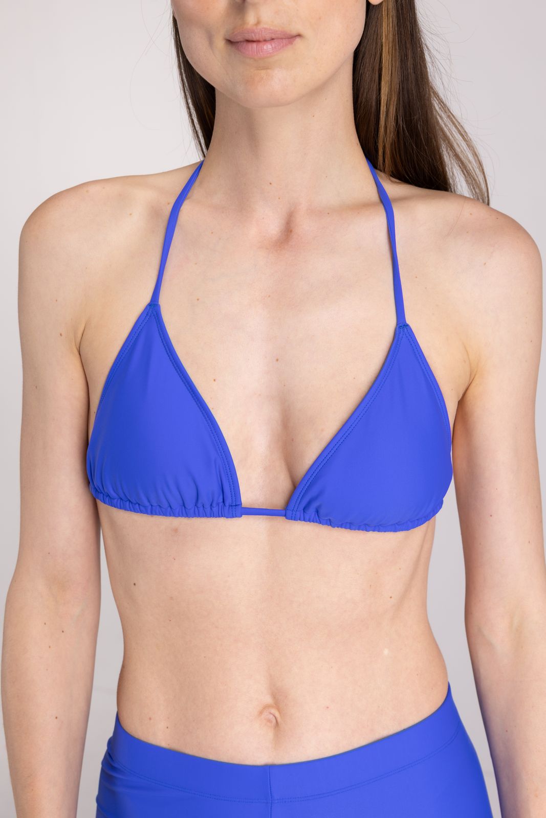 Close-up of cobalt blue triangle bikini top with halter tie, highlighting textured fabric, on light studio background