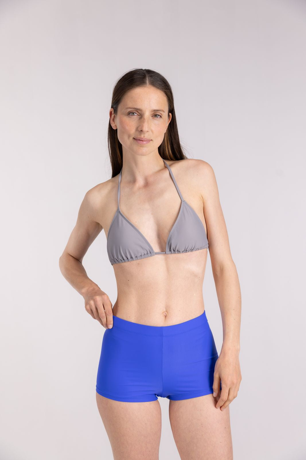 Seal grey bikini top styled for active beachwear, model in standing pose with cobalt shorts, light backdrop studio setting