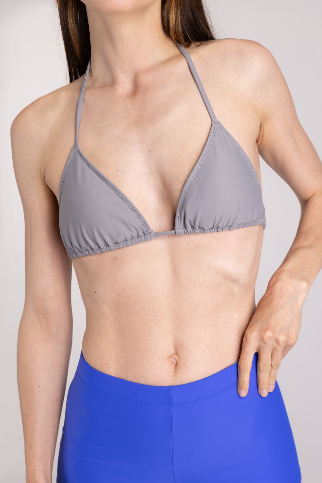 Close-up of seal grey triangle bikini top on model with soft gathering and halter tie, sustainable swimwear studio background