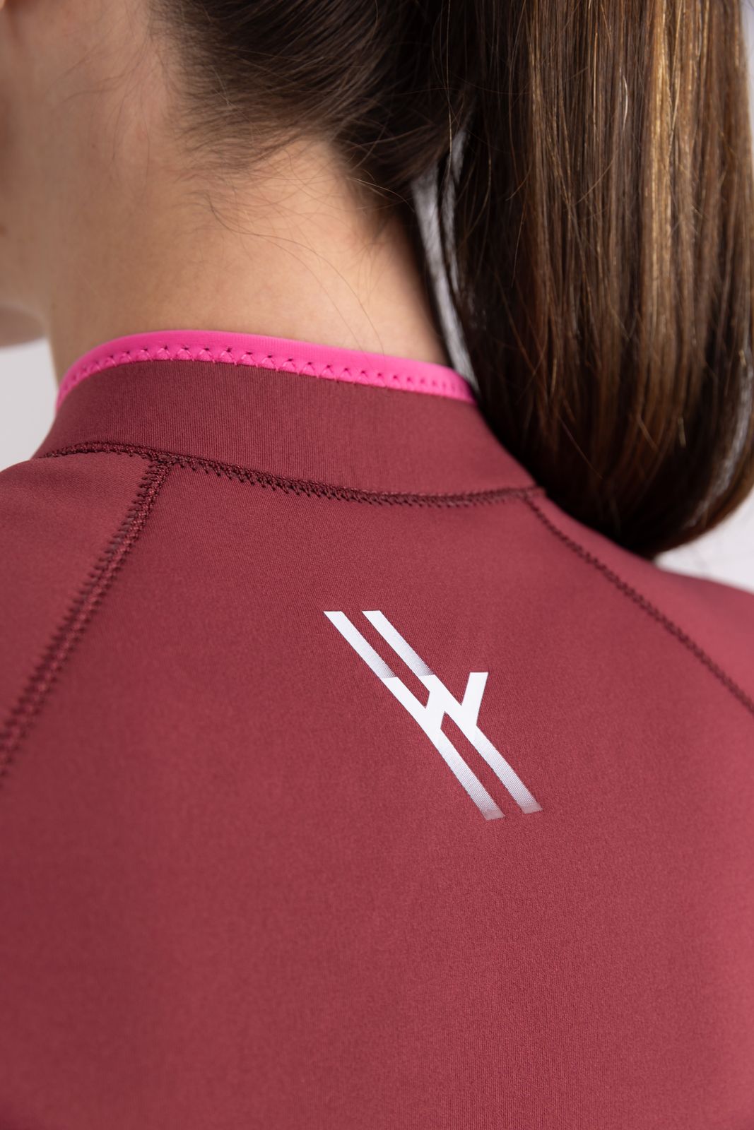 Close-up of red Yulex® surf jacket showing WALLIEN's eco-conscious GBS stitching, logo and rubber texture in white background