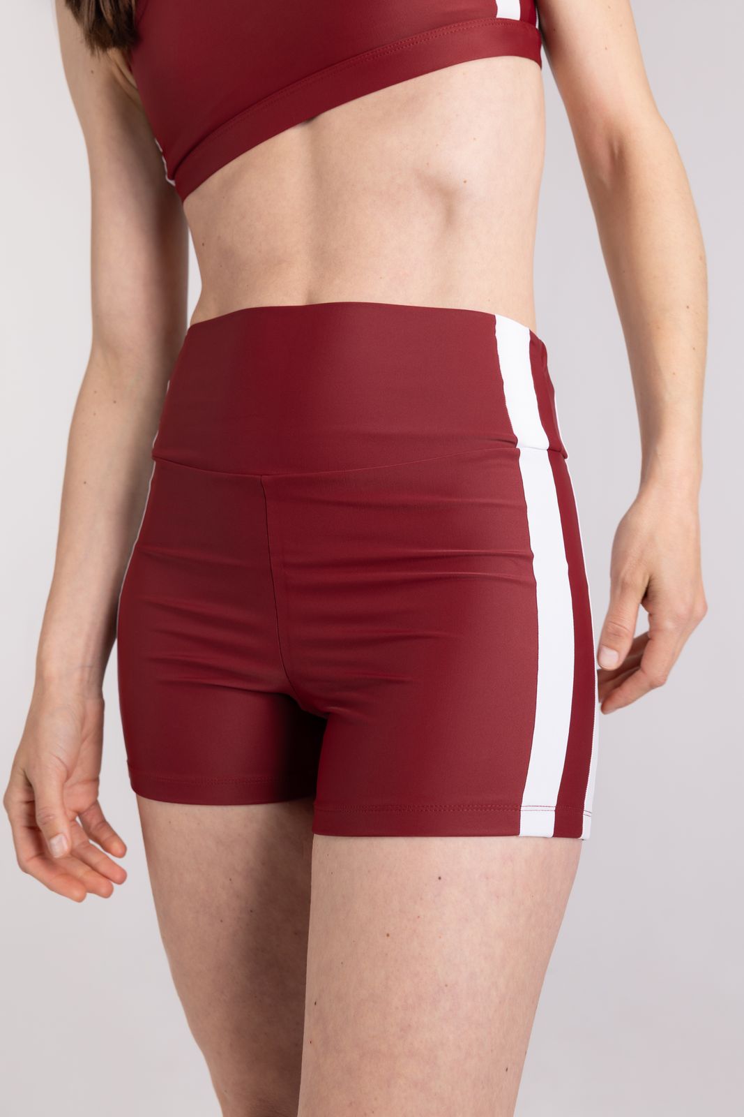 Close-up of high-rise red WALLIEN sports shorts with vertical white stripe, styled for movement, shot in studio background
