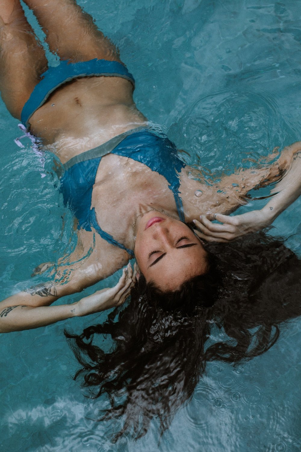 Woman floating in pool in teal-green bikini top, designed for water sports and eco-friendly swim sessions