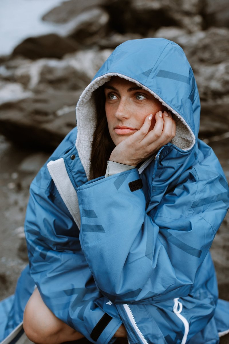 Relaxing in cozy WALLIEN blue changing robe after cold water swim, seated on rocks with coastal background