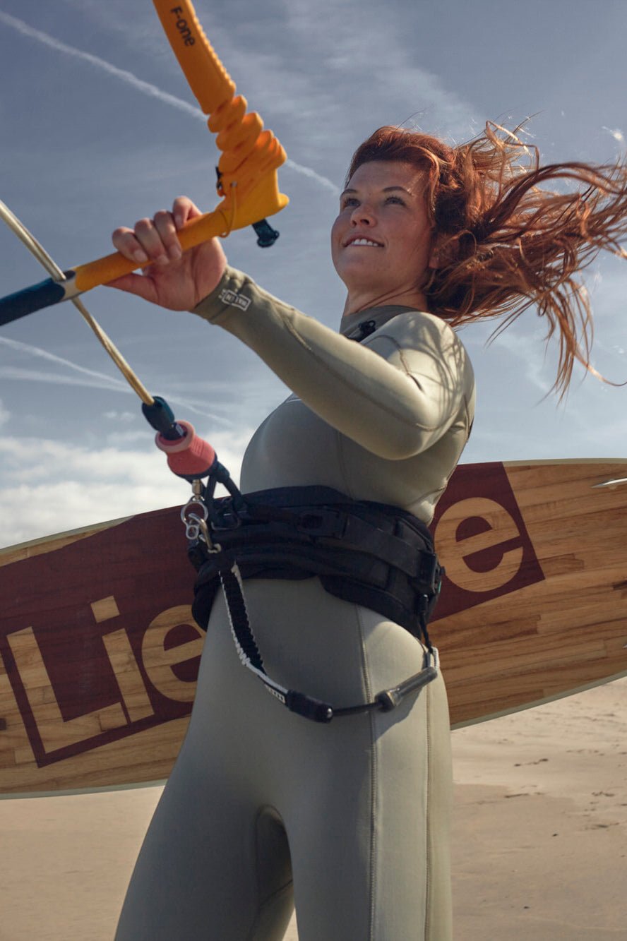 Woman kitesurfing in Nikki van Dijk 4/3 wetsuit on a windy beach day, for watersports with board and sky trails in background