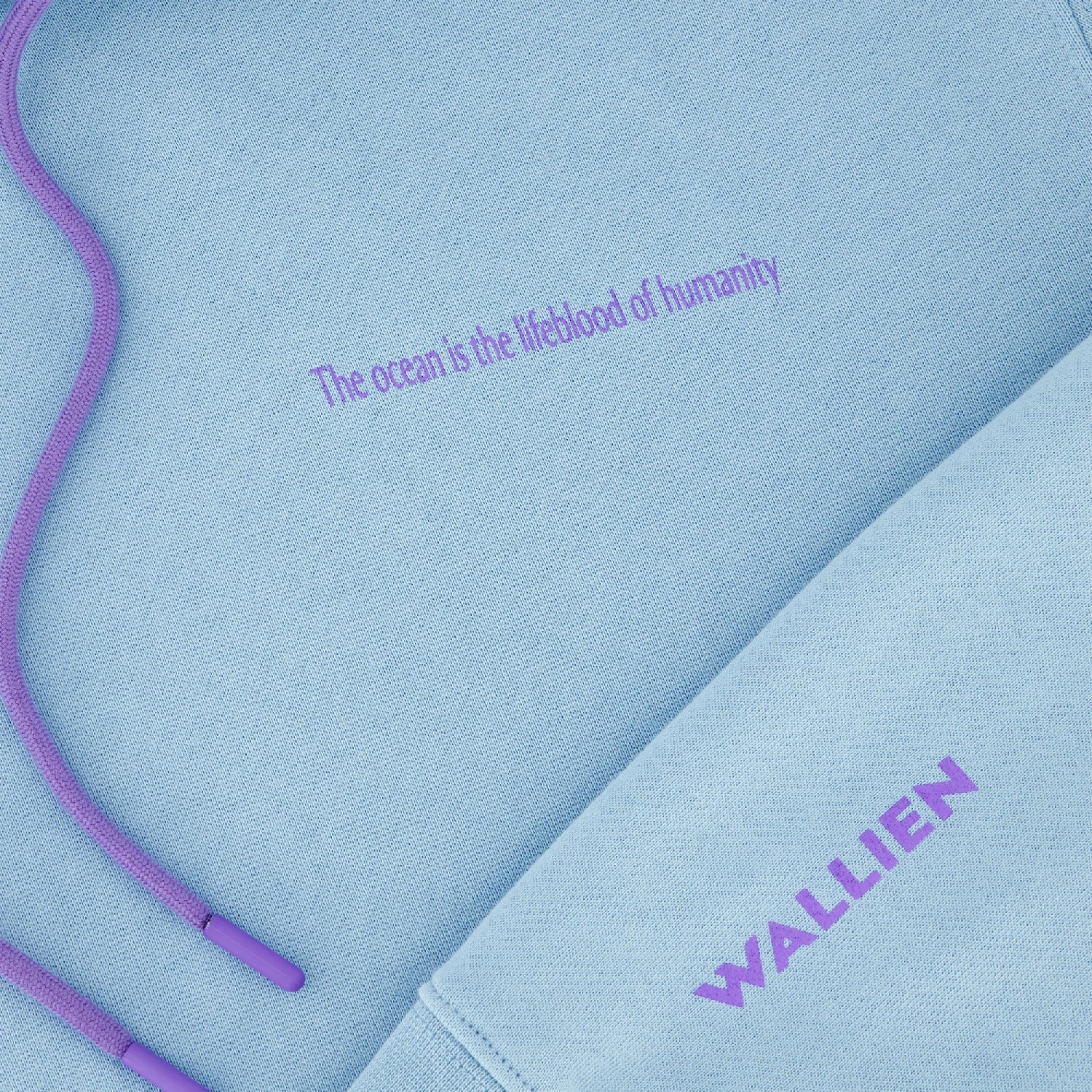 Close-up of blue Ocean Hoodie showing lavender drawstrings, chest slogan “ocean is lifeblood of humanity,” and WALLIEN logo