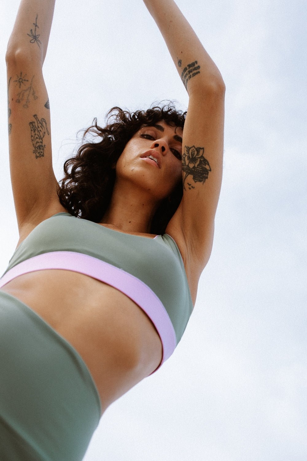 Low angle of woman in green sport shorts raising arms on beach, designed for surfing and beach workouts, sky in background