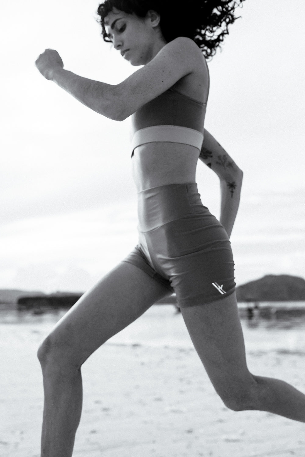 Woman sprinting on sand in green active sport shorts, designed for high-intensity water sports, island coast in background