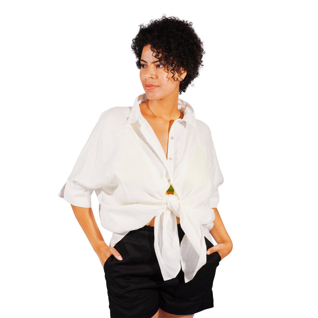 Woman styling WALLIEN off-white blouse with black shorts for relaxed beach look, flowy hem, soft fabric on studio background